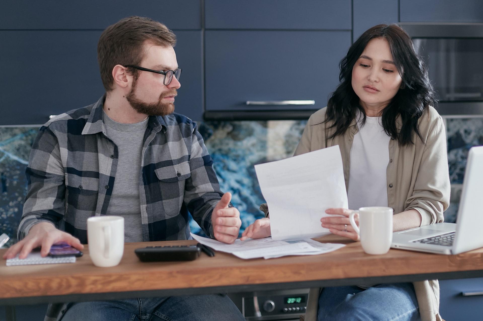 An unhappy woman and a man talking at a desk while going through paperwork.