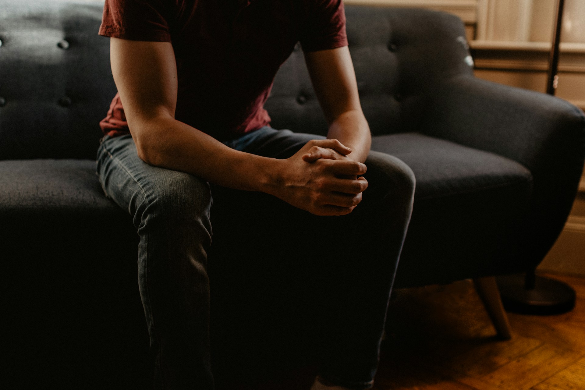 A person sitting on a couch with hands together, considering the consequences of drug offenses 